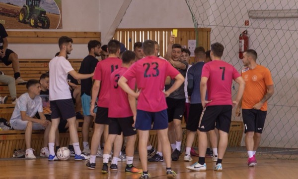 Jucători în tricouri roz și negre în jurul arbitrului, care arată un cartonaș galben